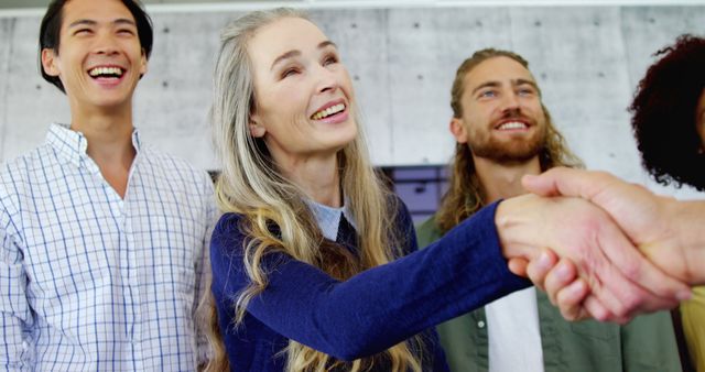 A group of diverse team members in casual attire seen smiling while one is shaking hands with another person. This conveys positive workplace dynamics, teamwork, and successful collaboration. Ideal use for business, partnership, and diversity inclusion concepts.