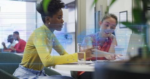 Women collaborating over laptop with digital data overlay in modern coworking workspace