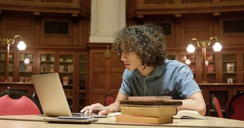 Young student studying in historic library with books and laptop