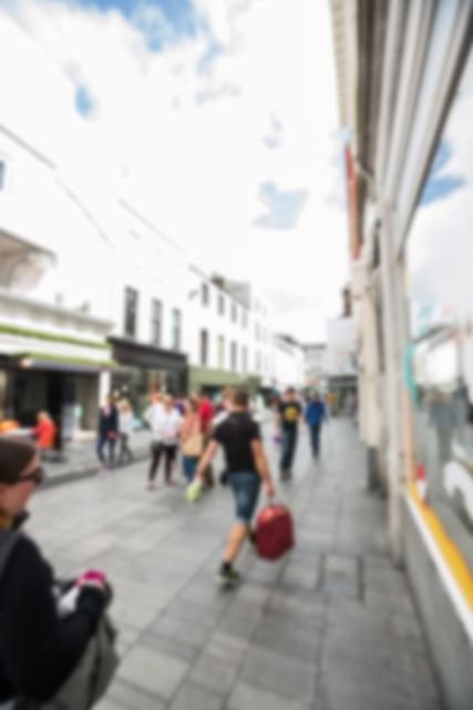 Blurred view of people casually walking on a city street during a sunny day. Suitable for themes of urban life, cityscape, daily commute, or travel.