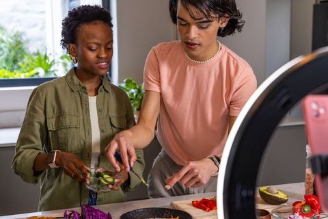 Diverse friends making salad while recording cooking video with ring light and smartphone