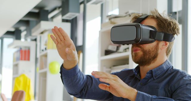 Bearded man exploring virtual reality with a VR headset in a modern office environment. Ideal for illustrating concepts of modern technology, virtual environments, digital interactions, innovative work settings, and tech enthusiasm.