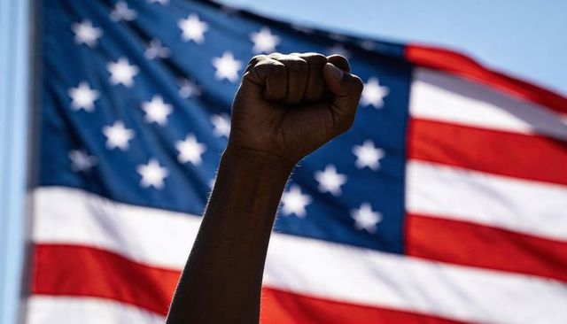 Raising dark-skinned clenched fist in front of american flag for protest solidarity