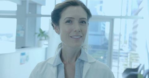 Female doctor standing and smiling in bright modern clinic lobby wearing white lab coat