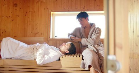 Couple relaxing in wooden sauna wearing bathrobes enjoying spa retreat and warm daylight