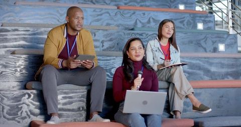Diverse professionals on panel using laptop, microphone and tablet in modern tiered seating