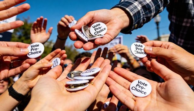 Hands passing vote pro-choice buttons at outdoor rally, closeup activism exchange