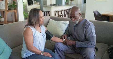 Homecare nurse measuring blood pressure for patient on sofa during home visit