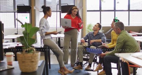 Woman presenting with laptop leading inclusive team meeting in modern open-plan office