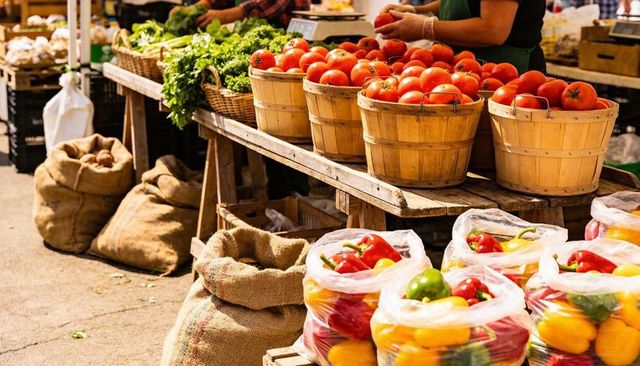 Displaying ripe tomatoes in wooden bushels at sunlit farmers market with colorful peppers