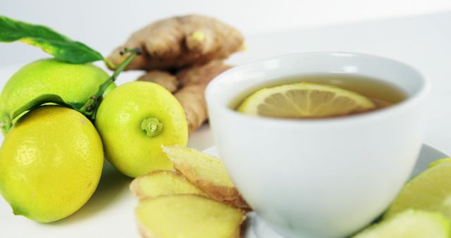This close-up view of a cup of lemon ginger tea accompanied by fresh ingredients can be used in various contexts. It is ideal for promoting healthy lifestyle choices, herbal tea products, and wellness blogs. The vibrant colors and fresh ingredients make it suitable for websites and publications relating to health benefits, recipes, or holistic remedies.