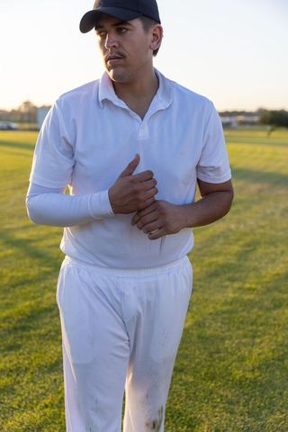 Cricket player adjusting wrist on sunlit grass field during golden hour practice