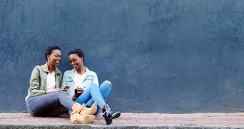 Twin Sisters Smiling and Using Mobile Phone on City Sidewalk