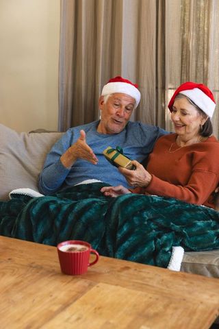 Senior couple in santa hats sharing gift in cozy living room