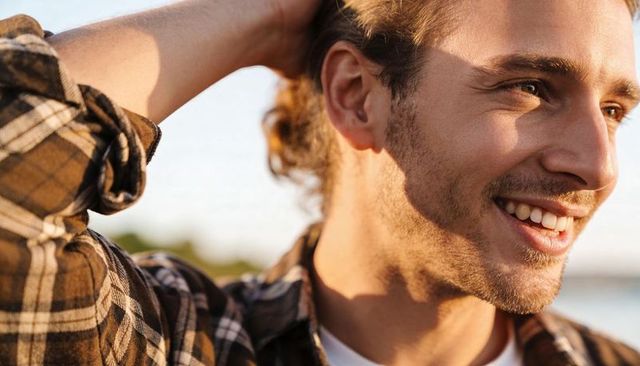 Smiling young man with bun at lakeshore during golden hour wearing plaid shirt casual portrait
