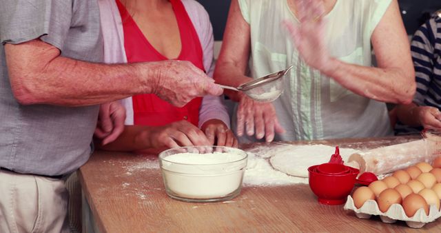 Family members working together baking at table in kitchen, sifting flour into bowls for dough making. Hands collaborating in cooking process, creating sense of togetherness and teamwork. Useful for advertisements focusing on family bonding, cooking products, baking tutorials, or homemaking themes.