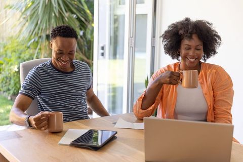 African american couple enjoying remote work and coffee at sunlit dining table with laptop