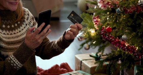 Senior Woman Online Shopping by Christmas Tree with Mobile Phone