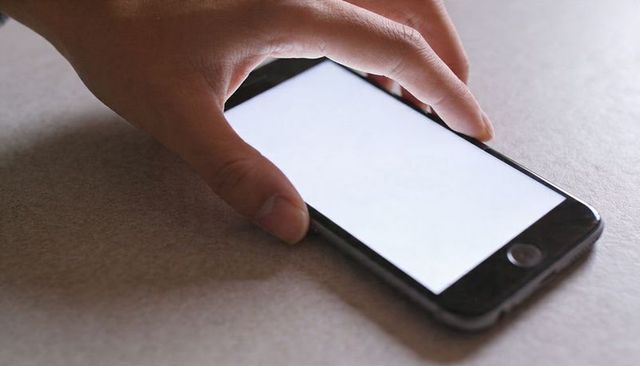 Hand Tapping Smartphone with Blank Screen on Neutral Tabletop for App Mockups