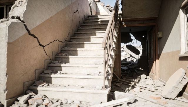 Collapsed concrete stairwell with exposed rebar and rubble, sunlit ruin interior