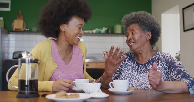 This picture shows a joyful moment of a grandmother and granddaughter bonding at a kitchen table, sharing stories over coffee and cookies. Ideal for use in family-oriented advertisements, blogs about family relationships, articles on aging and multi-generational living, and websites focused on home and lifestyle content.
