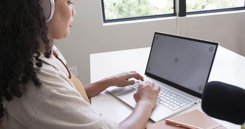 African american woman working on laptop with headphones at minimalist home office desk