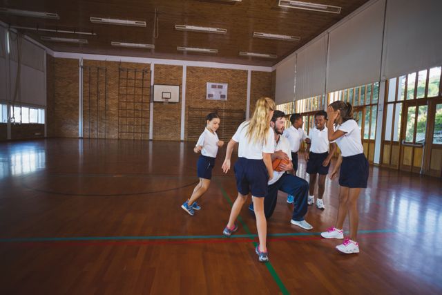 Sports teacher and school kids playing basketball in court at school gym