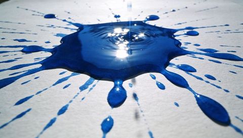 Cobalt blue splash with central ripple and glossy radial splatters on textured paper