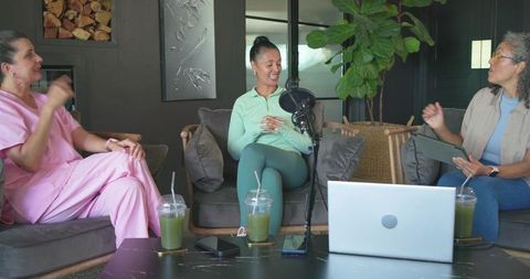 Three women recording podcast conversation in cozy home studio with green smoothies