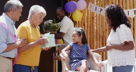 Multigenerational family celebrating backyard birthday with grandparents giving gift to young girl