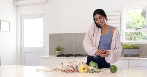 Woman sorting fresh vegetables with reusable bags in bright kitchen