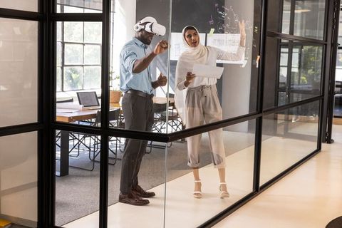 Diverse Coworkers Using VR Headset and Printed Plans in Modern Office