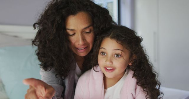 Biracial mother and daughter sitting in bedroom and looking at something. domestic life and leisure time concept.