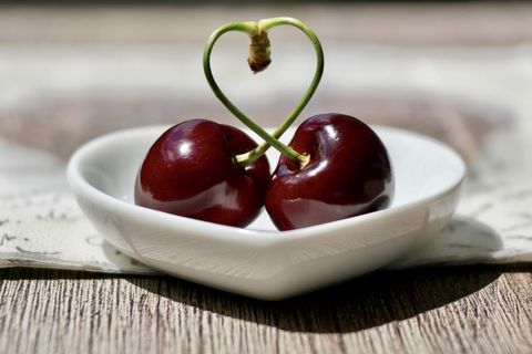 Cherry background with stems forming heart on white dish
