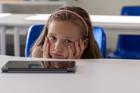 Bored schoolgirl waiting during digital lesson with tablet on desk in modern classroom