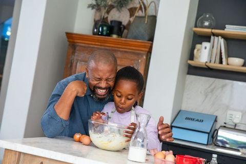 African american father laughing with daughter while whisking batter in bright kitchen