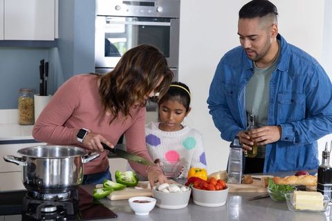 Asian family cooking together at kitchen island preparing healthy vegetable meal for kids