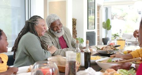 Senior African American couple laughing and sharing meal at multigenerational family table