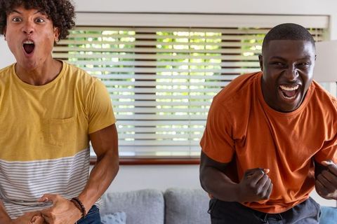 Young diverse friends cheering and celebrating while watching game on couch at home