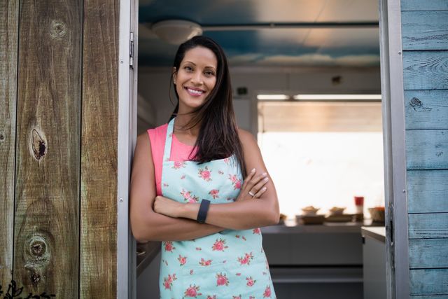 Portrait of happy waitress standing with arms crossed at the entrance of food truck