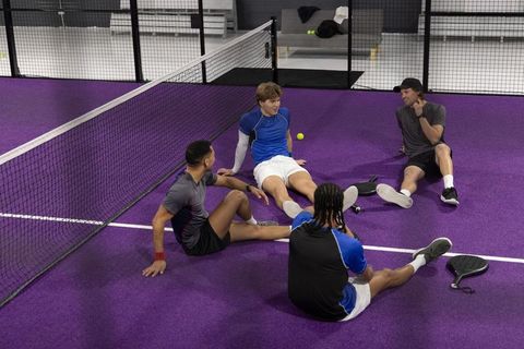 Multiracial men sitting and talking on purple indoor pickleball court showing camaraderie
