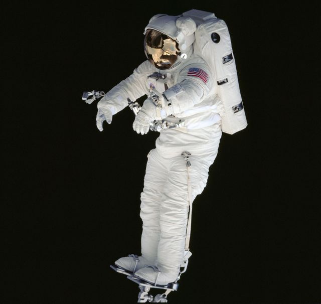 An astronaut is floating in the blackness of space while attached to the Space Shuttle Endeavour's Remote Manipulator System (RMS). The astronaut's suit, adorned with an American flag patch, appears illuminated against the dark backdrop. This image, captured with 70mm film using a Hasselblad camera, showcases a real-life spacewalk. Useful for illustrating space exploration, human spaceflight, NASA missions, and educational content about astronaut activities.