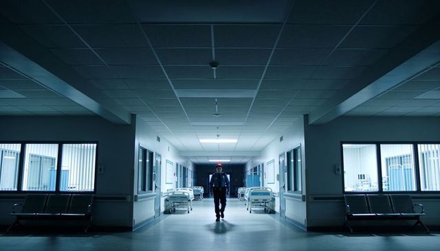 Night hospital security guard patrolling empty clinical corridor with patient beds