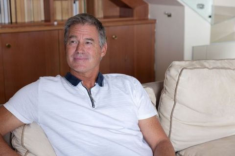 Mature man relaxing on beige sofa in modern living room wearing white polo