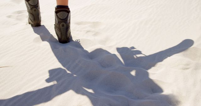 Person walks on sandy terrain, casting a long shadow. Outdoor adventure is captured with a focus on exploration and solitude.
