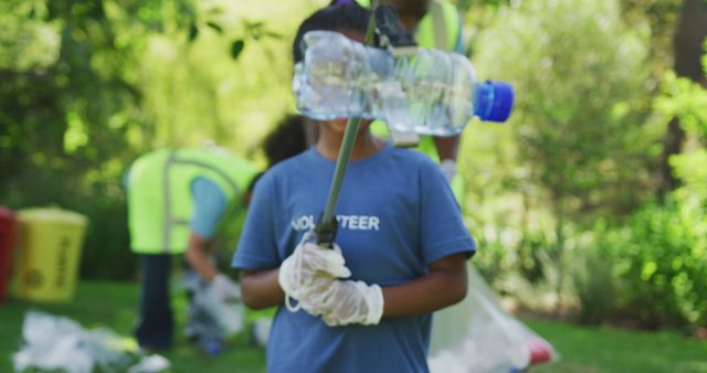 Biracial girl in volunteer t shirt holding plastic bottle, clearing up trash outdoors with family. Ecology, volunteering, recycling, nature conservation, family and togetherness.