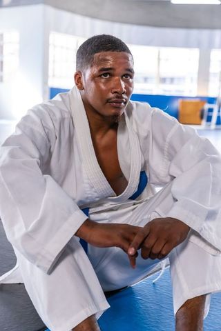 Martial Artist in White Gi and Blue Belt Resting on Blue Mat in Bright Dojo