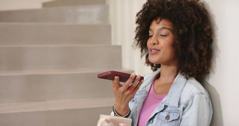 African American woman speaking into smartphone sitting on staircase holding coffee mug