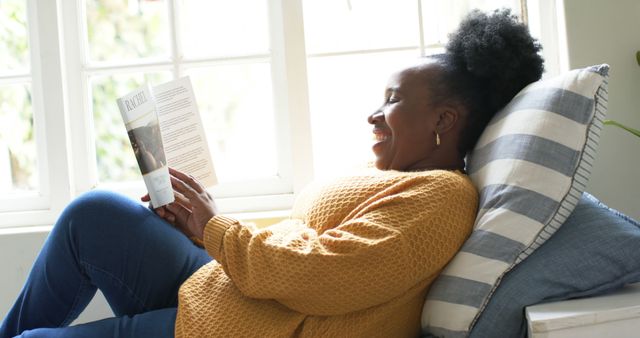 Smiling woman reading book by window on cozy afternoon - Download Free Stock Images Pikwizard.com