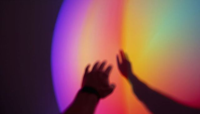 Hand reaching toward rainbow gradient light with shadow and wristband, immersive color scene